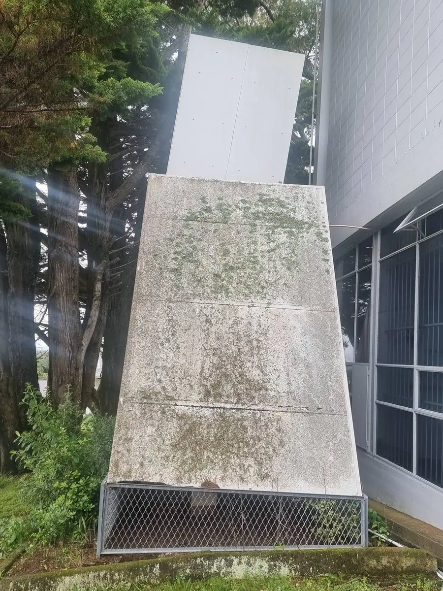 Asbestos-cement ventilation hood mounted against the building wall, showing weathered fibre-cement panels