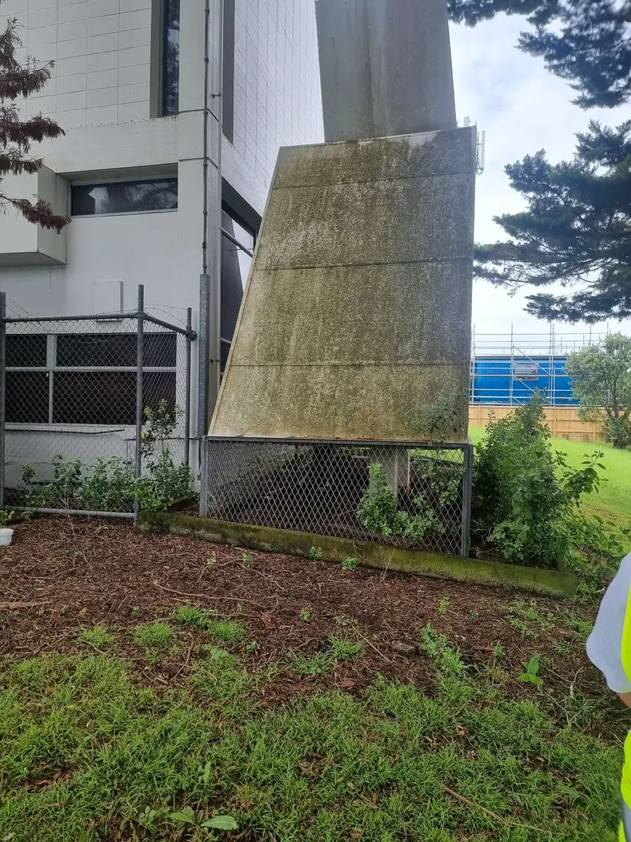 Asbestos-cement ventilation hood over a garden bed at a commercial site, with safety fencing behind