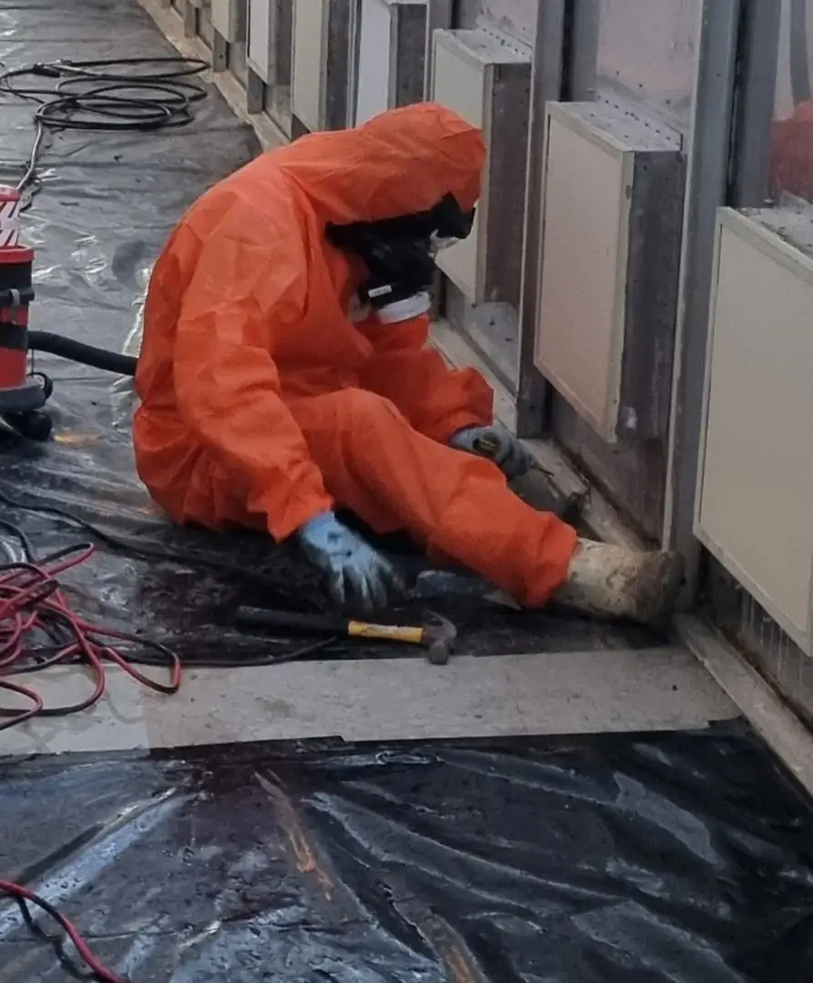 SES operative in orange PPE removing asbestos window sill boards in an office