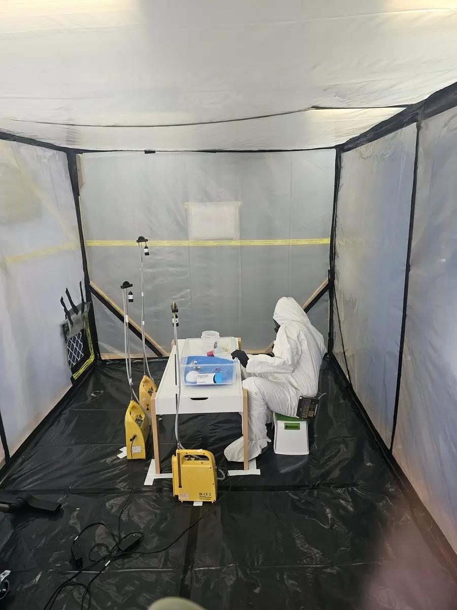 SES operative in white coveralls working inside the asbestos enclosure