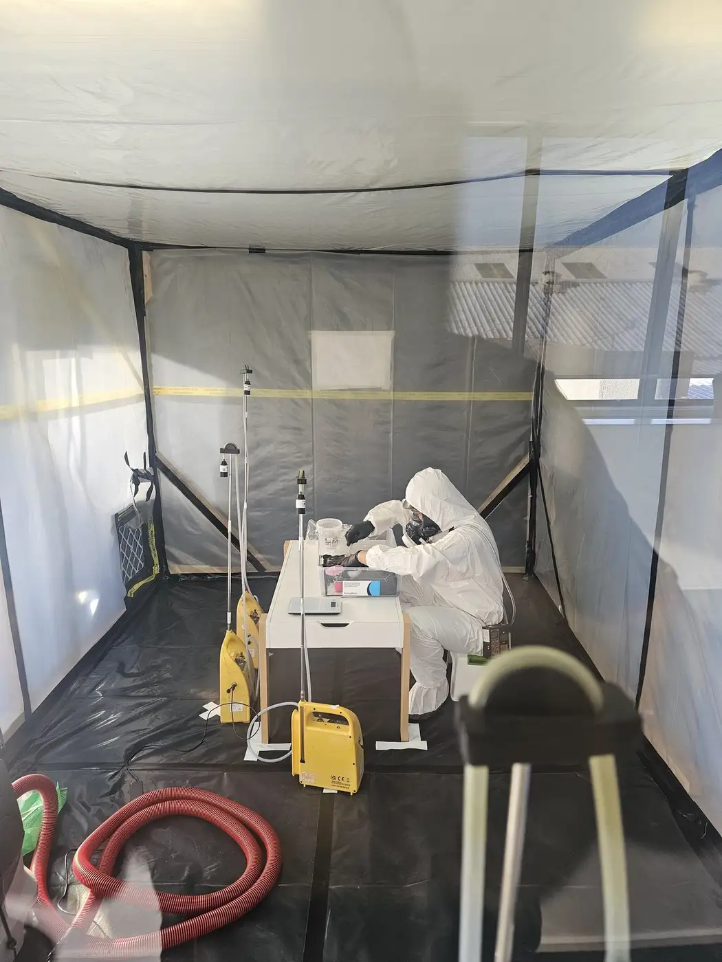 SES asbestos removal crew in PPE working at the bench inside the enclosure