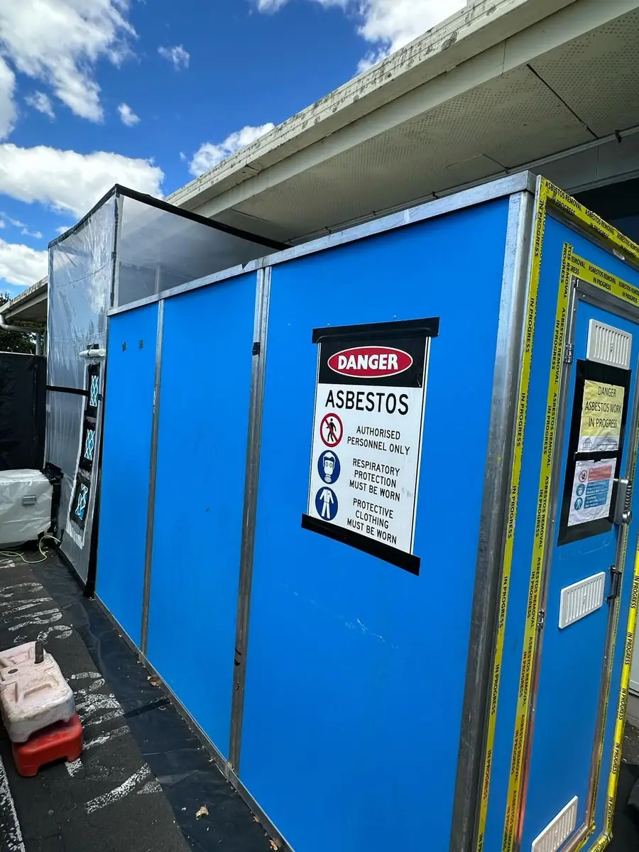 Blue decontamination unit with danger asbestos sign outside the building