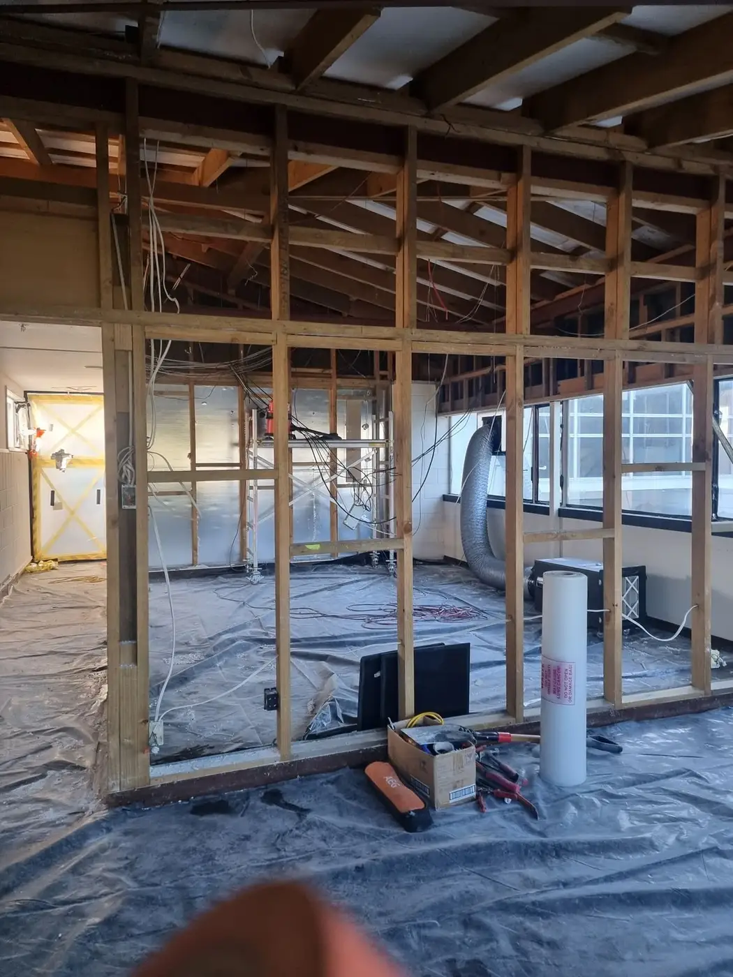 Office partitions stripped to framing with the floor sheeted in black poly