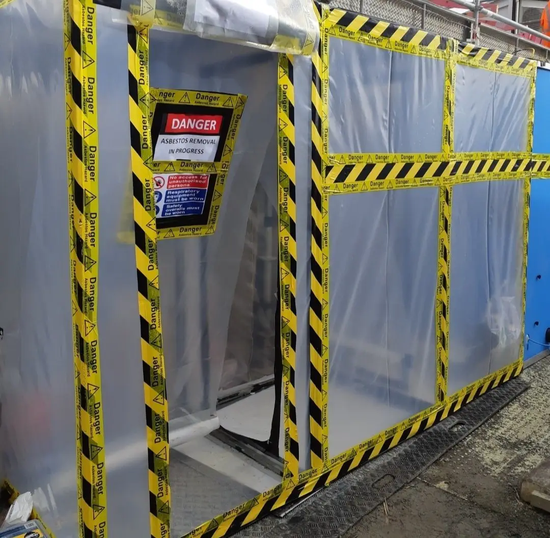 Residential asbestos enclosure with danger tape and decontamination unit