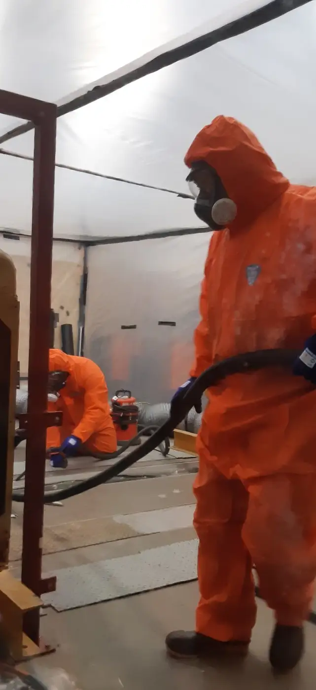 SES operatives in orange PPE HEPA vacuuming inside the enclosure